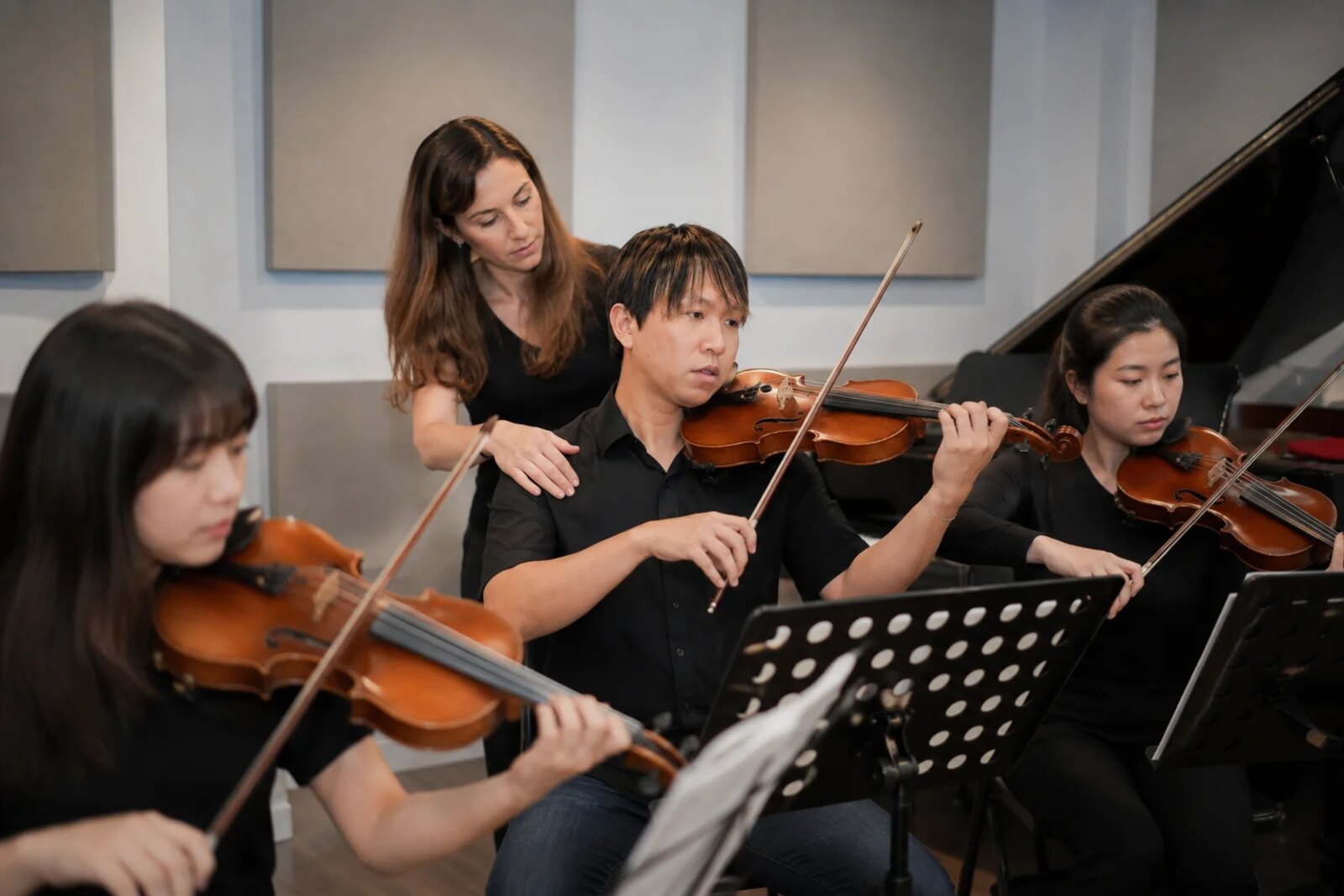 Three violinists playing at music stands while a fourth person guides them in a studio